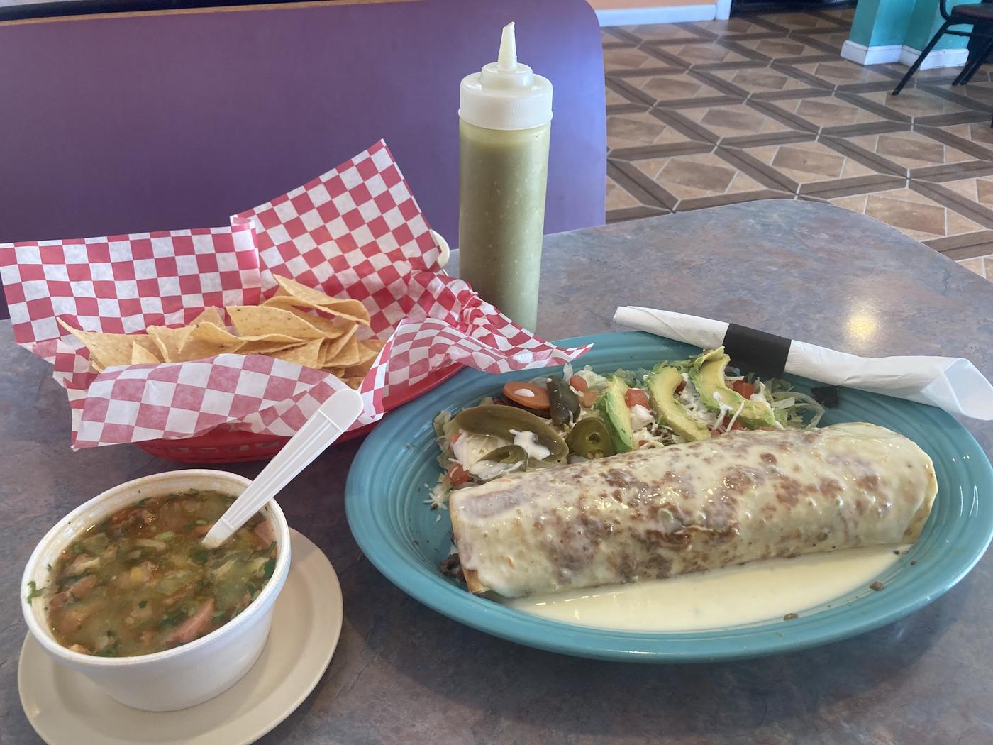 A burrito under white queso on a teal plate in our dining room